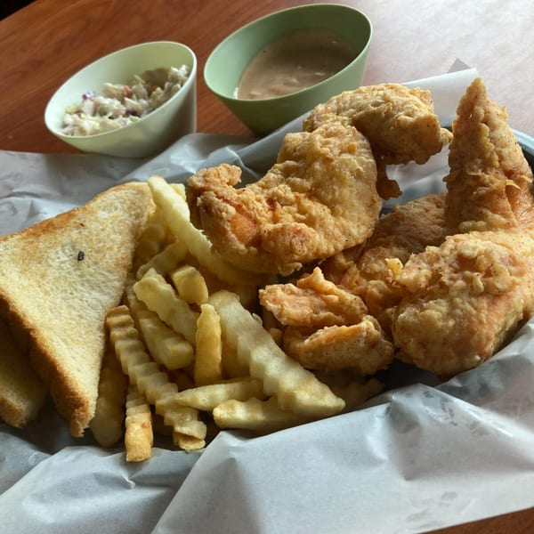 Barge Inn's fried chicken tenders, crinkle-cut fries, toast, coleslaw, and gravy on a wooden table.