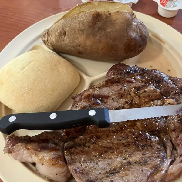A steak dinner with a baked potato, a dinner roll, and a steak knife on a plate.
