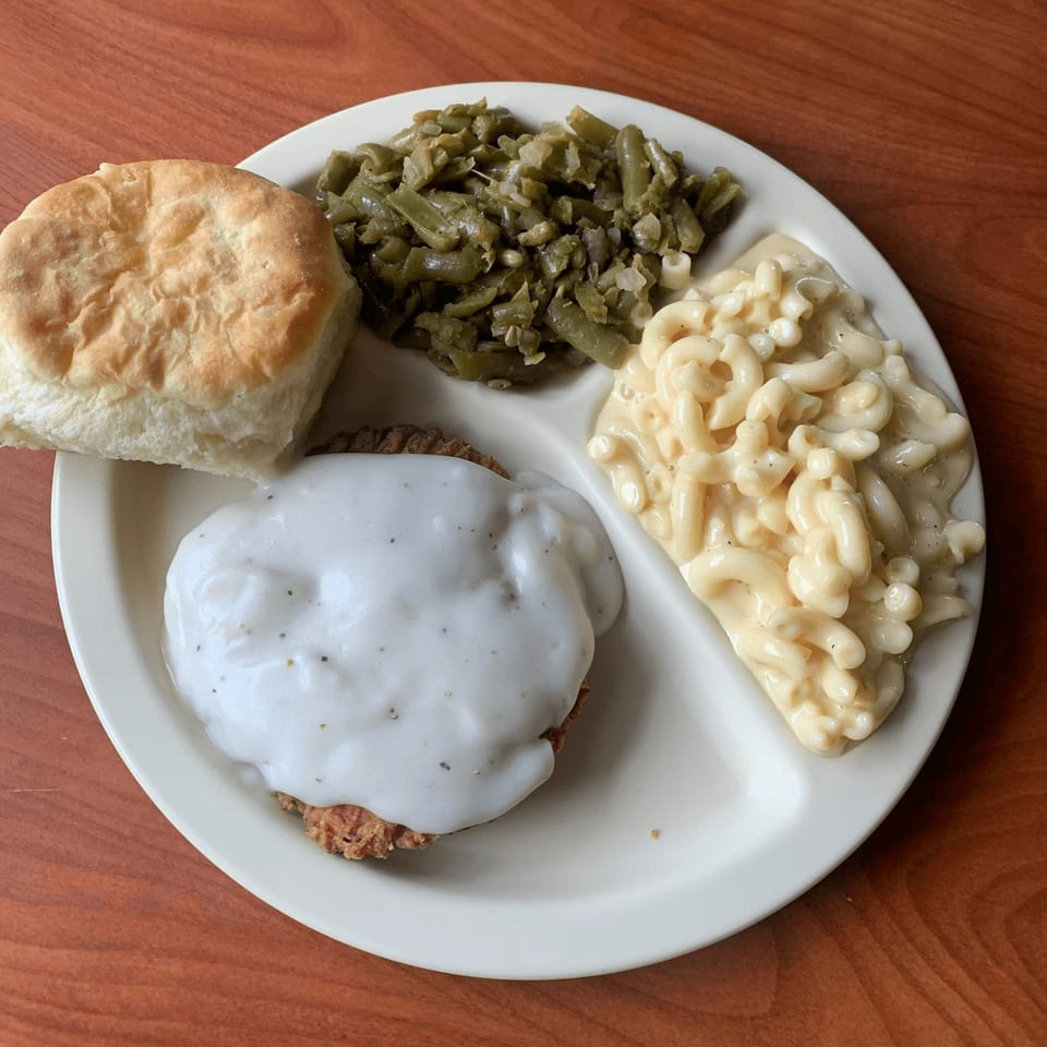 A Barge Inn American meal with country fried steak, gravy, green beans, macaroni and cheese, and a biscuit.